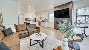 A modern living room with a brown leather sofa, a round coffee table, and a TV mounted on a wooden wall. - Flagstaff Group Getaway w/ Game Room & Deck (Flagstaff)