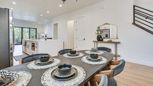 A modern dining area with a long table set for six, a kitchen in the background, and a staircase with a railing. - Flagstaff Group Getaway w/ Game Room & Deck (Flagstaff)