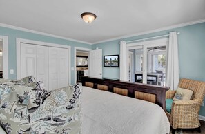 A bedroom with a large bed, a wicker chair, and a view of the outside.
