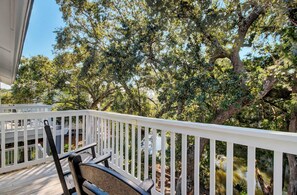 A wooden deck with a white railing, surrounded by lush greenery and trees.