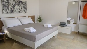 A modern hotel room with a large bed, a bedside table, a nightstand, a mirror, and a plant.
