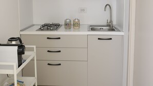 A compact kitchen with white cabinets, a stainless steel range hood, a sink, and a small shelf with jars.