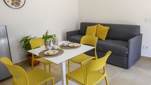 A small living area with a gray sofa, yellow cushions, a white table with yellow chairs, and a potted plant.