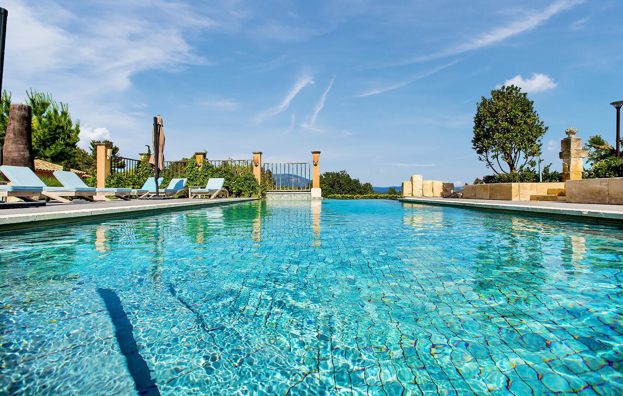 A clear swimming pool with lounge chairs and a view of the ocean.