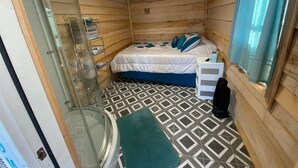 Um quarto pequeno e acolhedor, com cama, chuveiro e vaso sanitário.