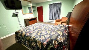 A bedroom with a bed, a dresser, a chair, a television, and a door. - Your Motel (Ypsilanti)