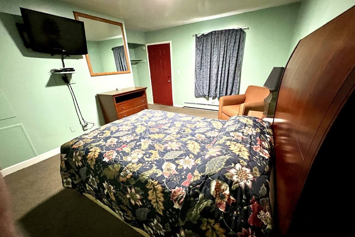 Une chambre à coucher avec un lit, une commode, une chaise, un téléviseur et une porte.