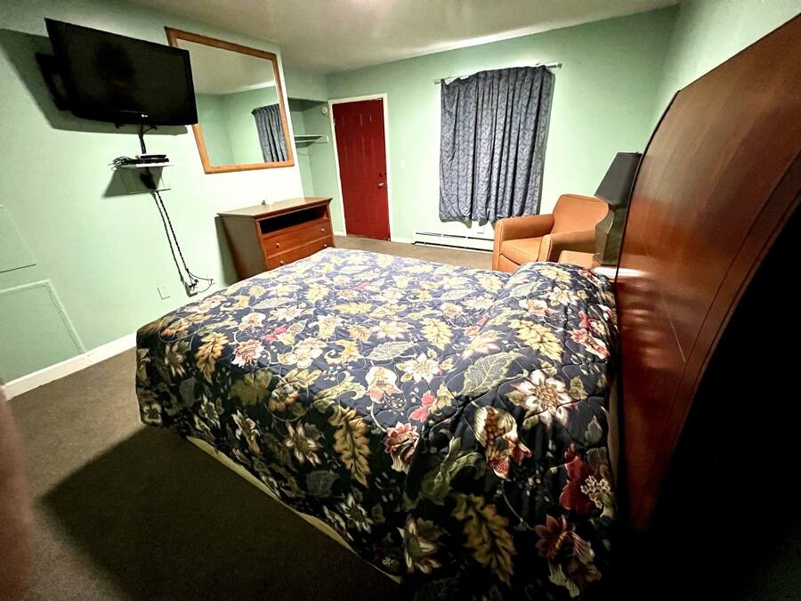 A bedroom with a bed, a dresser, a chair, a television, and a door.