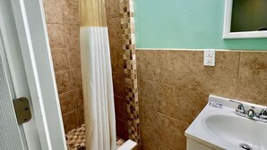 A bathroom with a shower, a sink, and a vanity. - Your Motel (Ypsilanti)