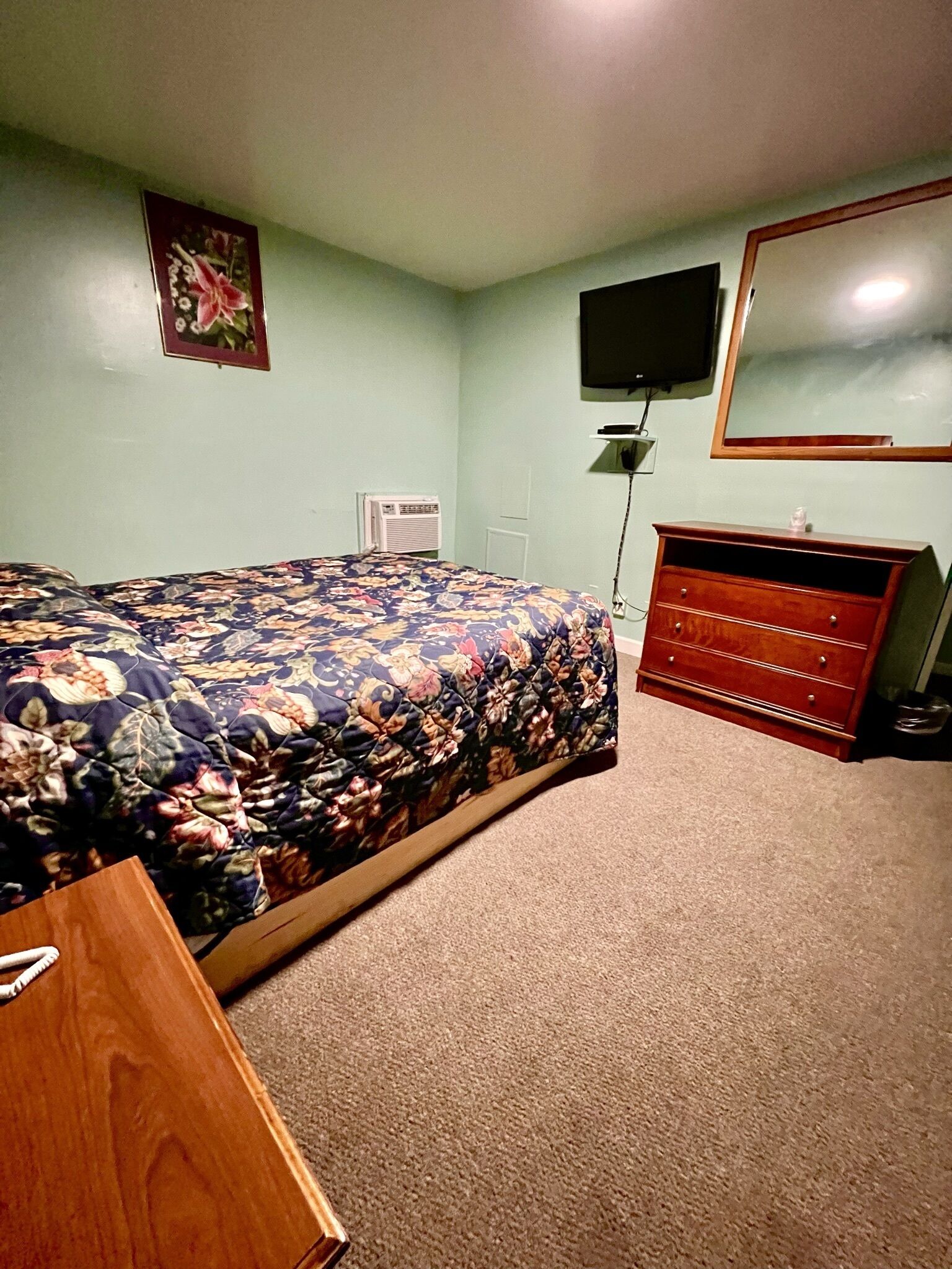 A bedroom with a bed, dresser, TV, and a picture on the wall.