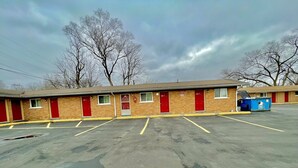 A motel with multiple red doors, a parking lot, and a blue dumpster. - Your Motel (Ypsilanti)