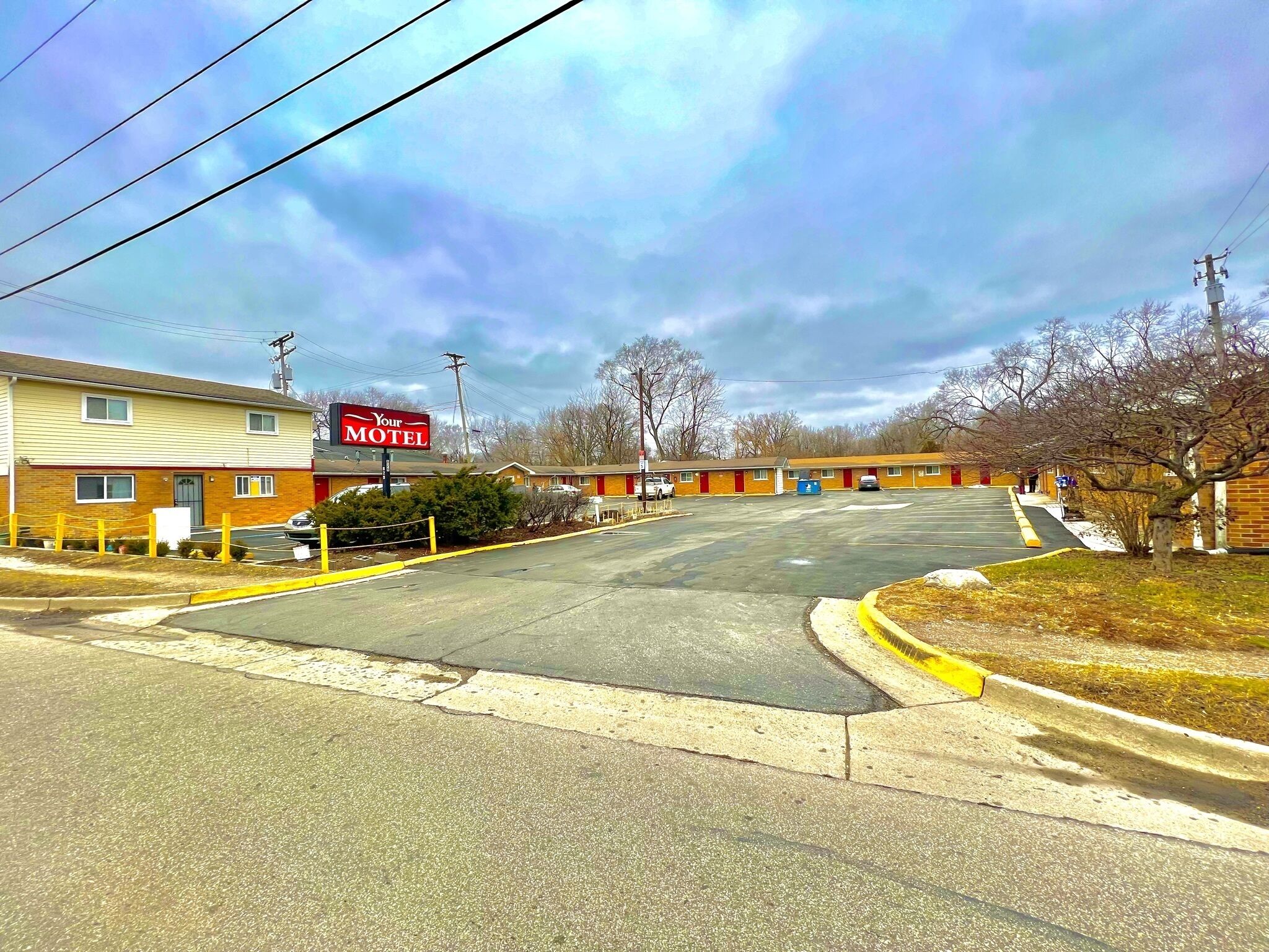 A motel with a large sign, a parking lot, and a building with a red door.