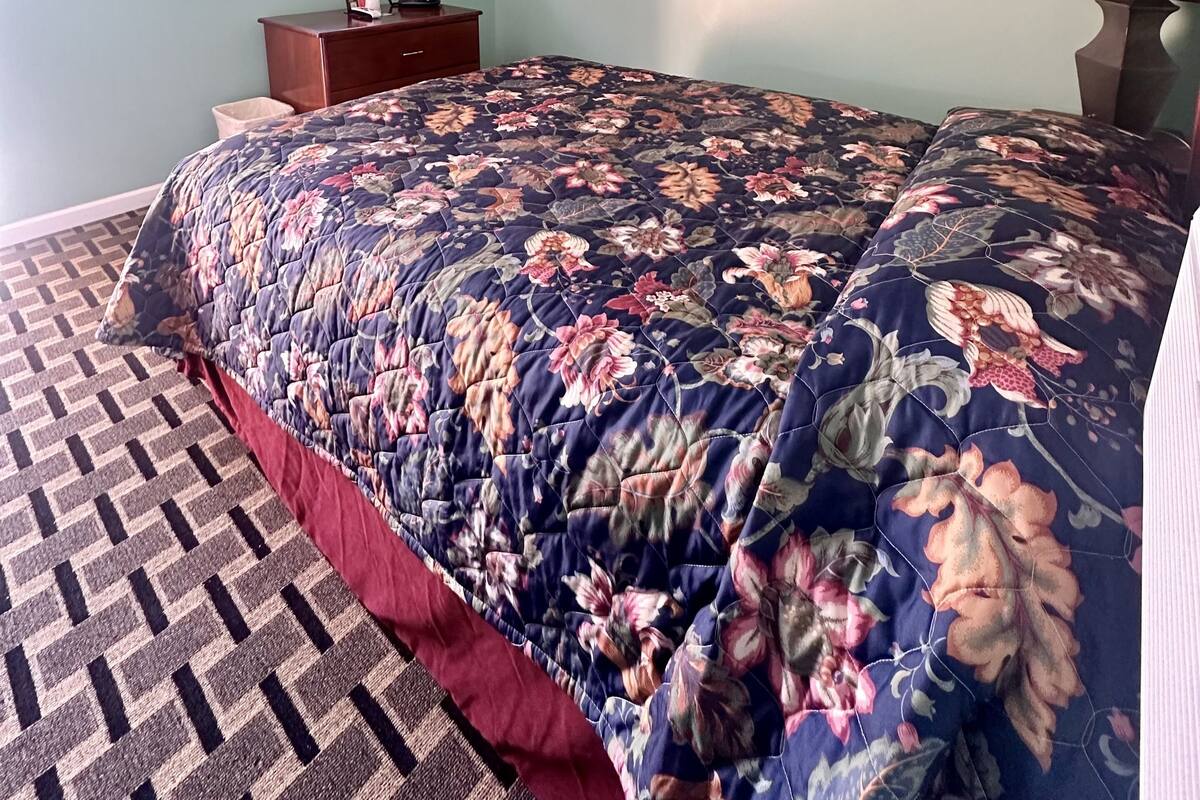 Une chambre à coucher avec une couvre-lit à motifs floraux, un téléviseur fixé au mur et un tapis à motifs.