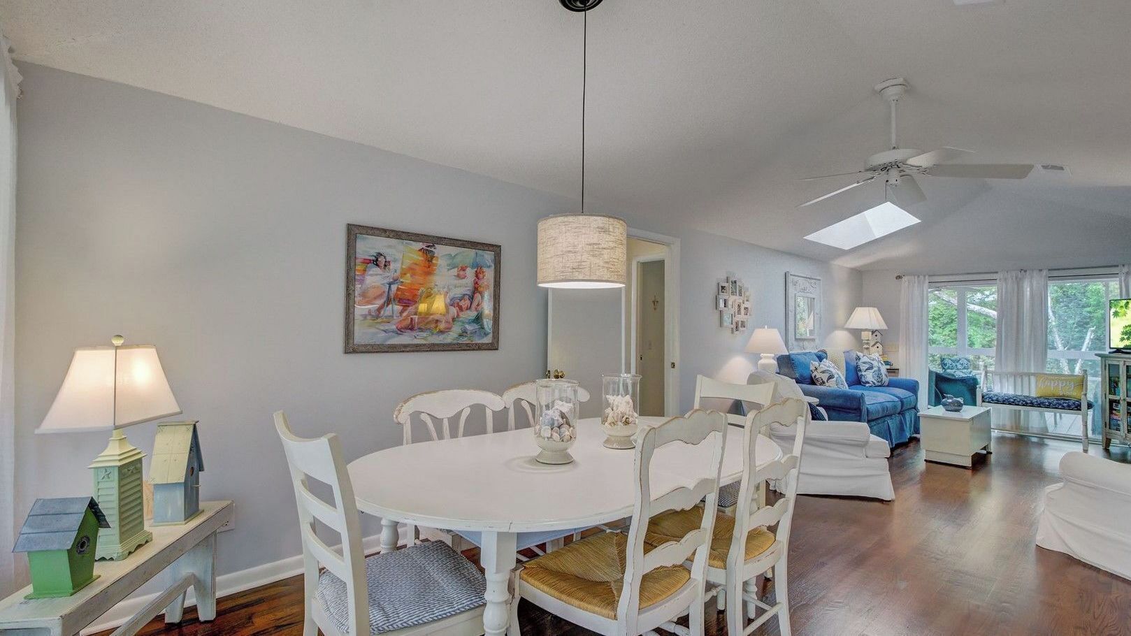 A dining area with a round table, white chairs, and a lamp. There is a blue sofa and a white chair in the background.
