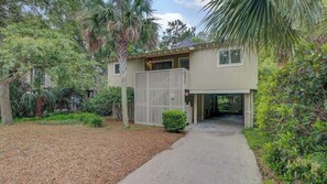 A two-story house with a covered driveway, surrounded by dense greenery and a well-maintained lawn.