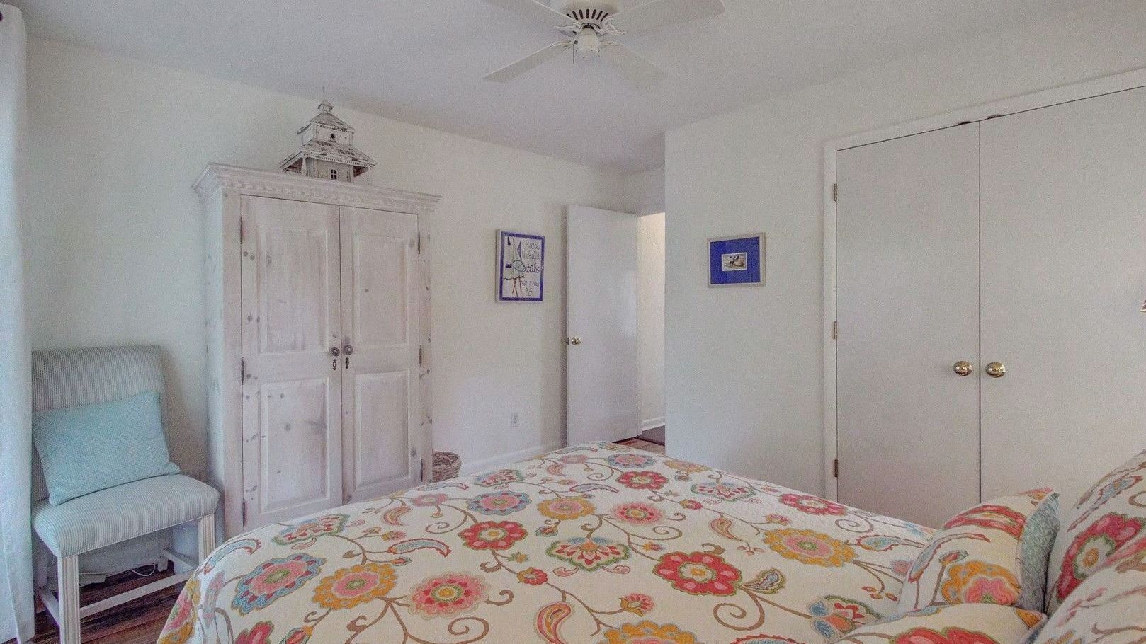 A bedroom with a bed, a chair, a wardrobe, and a ceiling fan.