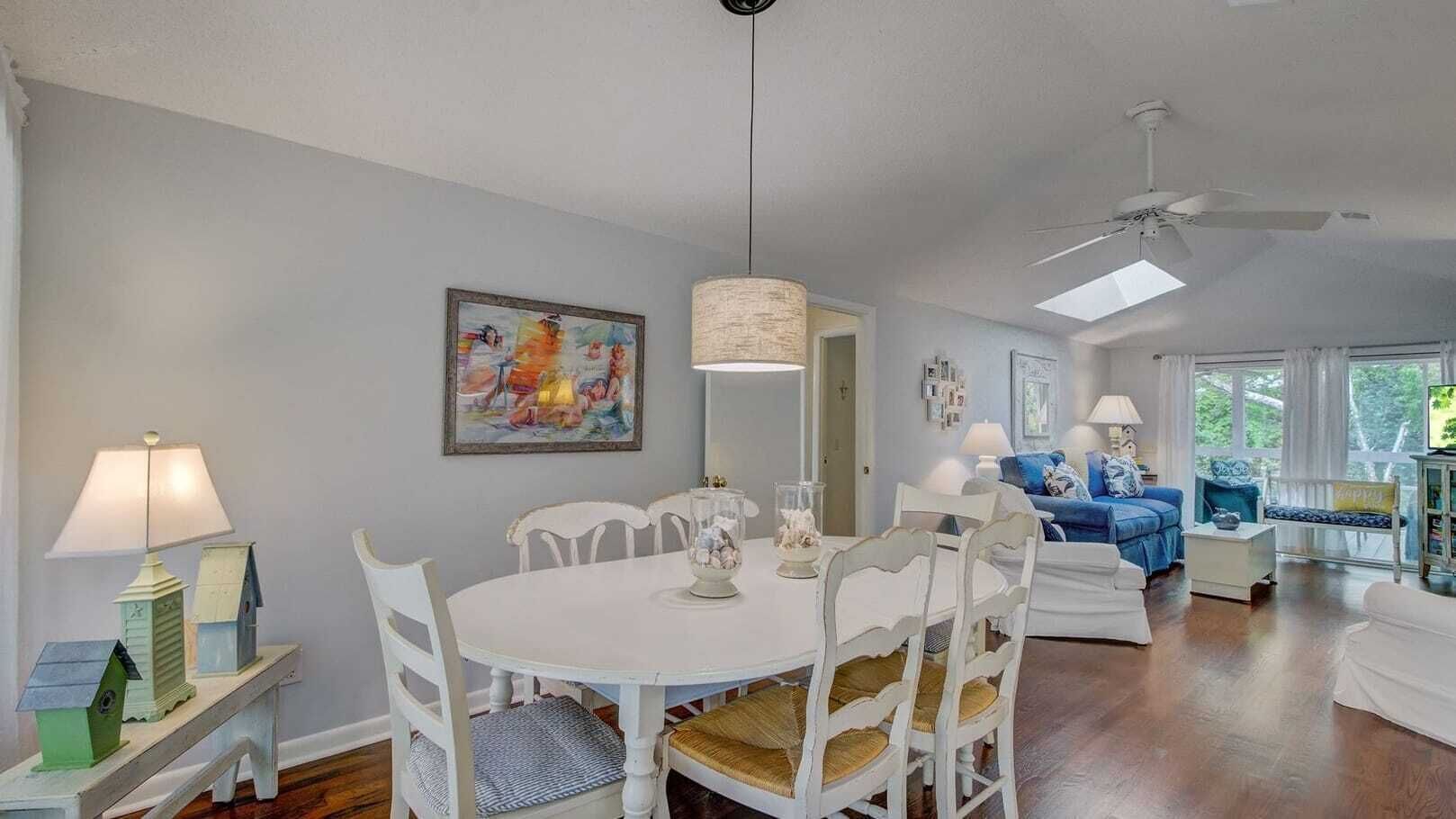 A dining area with a round table and white chairs, a blue sofa, and a ceiling fan.