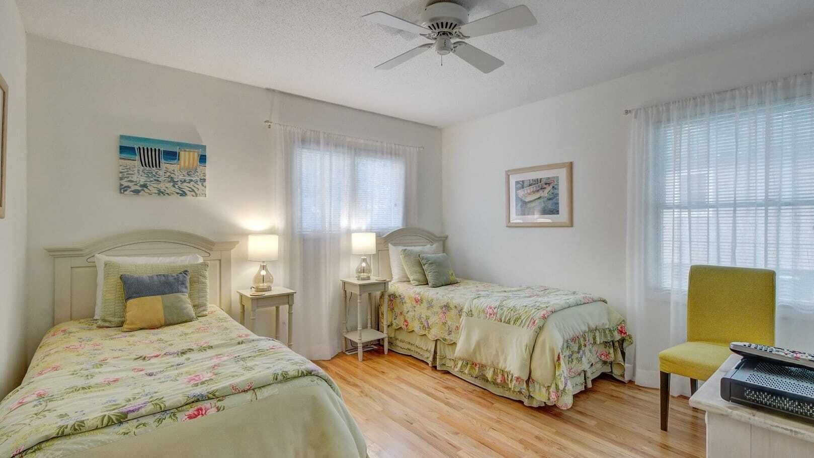 A bedroom with two single beds, a ceiling fan, and a chair.