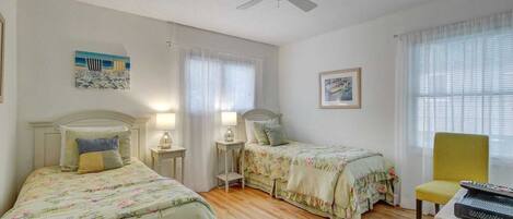 A bedroom with two single beds, a ceiling fan, and a chair.