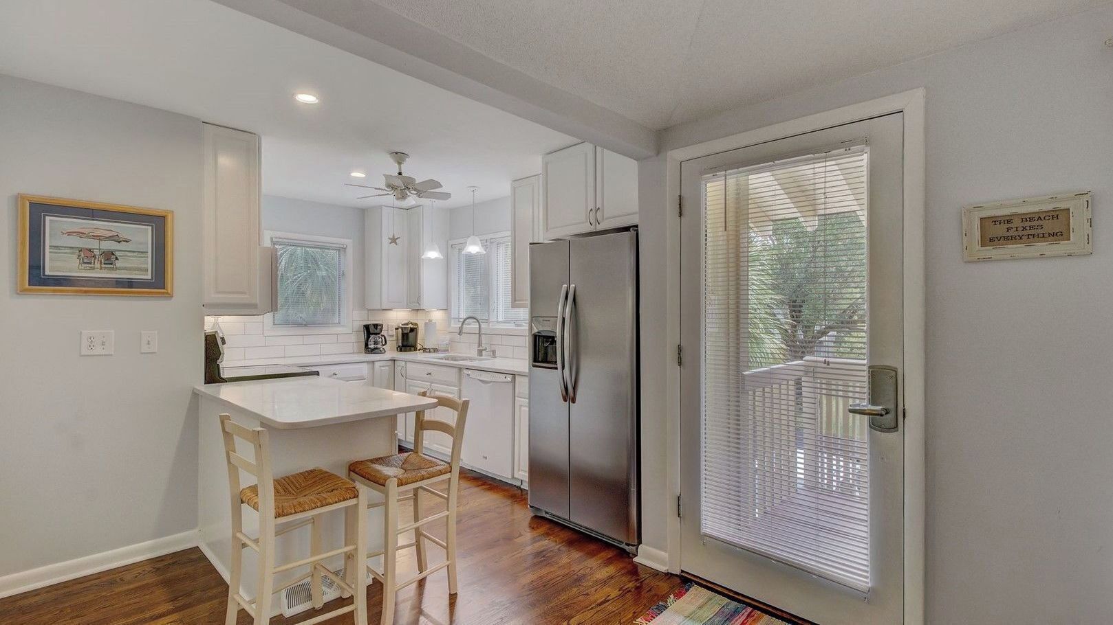 A kitchen with white cabinets, a stainless steel refrigerator, a dining table with two chairs, and a ceiling fan.