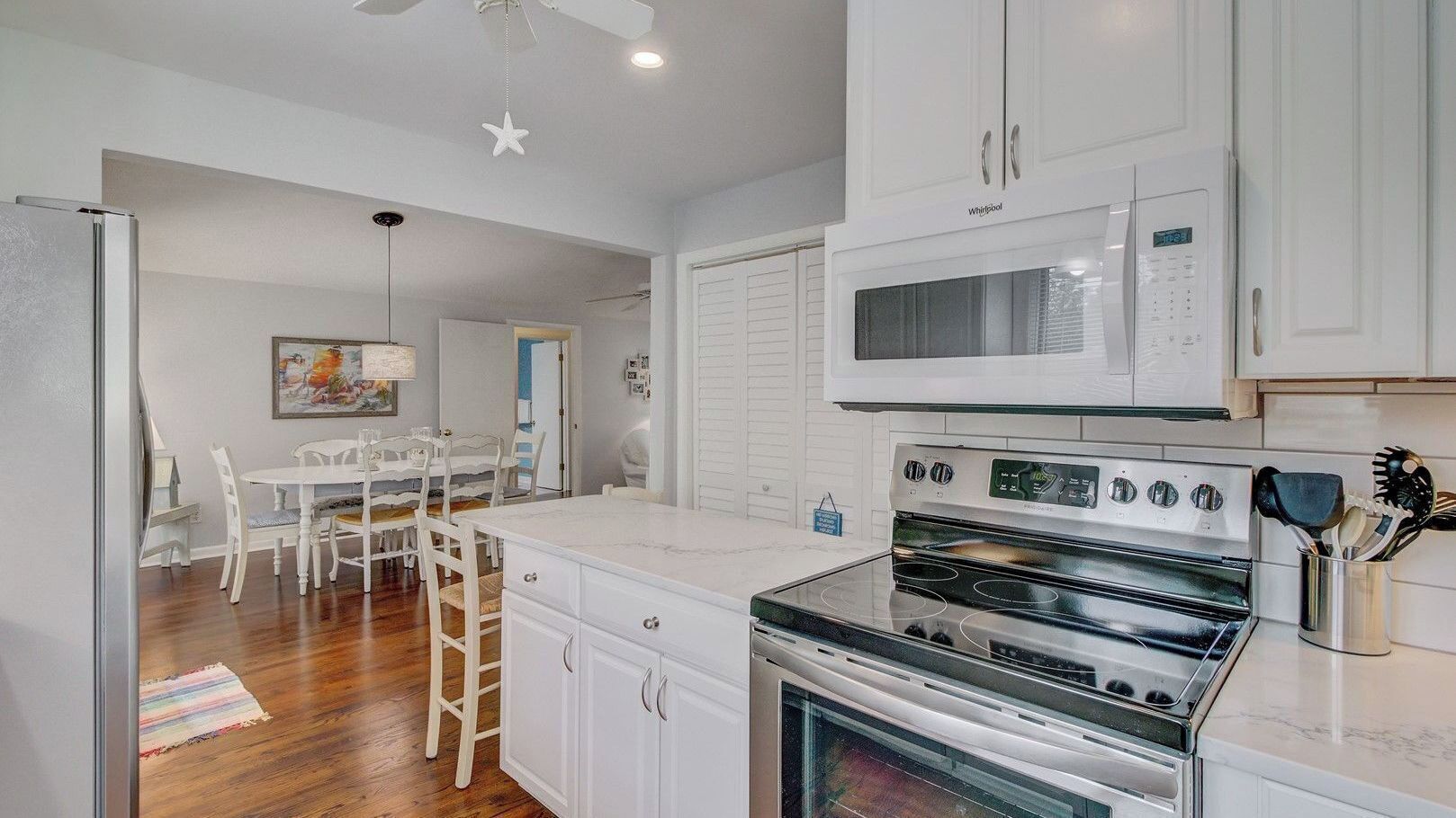 A kitchen with white cabinets, a microwave, an oven, and a dining area with a table and chairs.