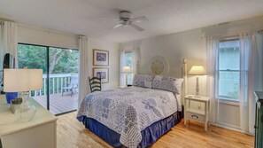 A bedroom with a bed, a ceiling fan, a nightstand, a lamp, a chair, and a window with curtains.