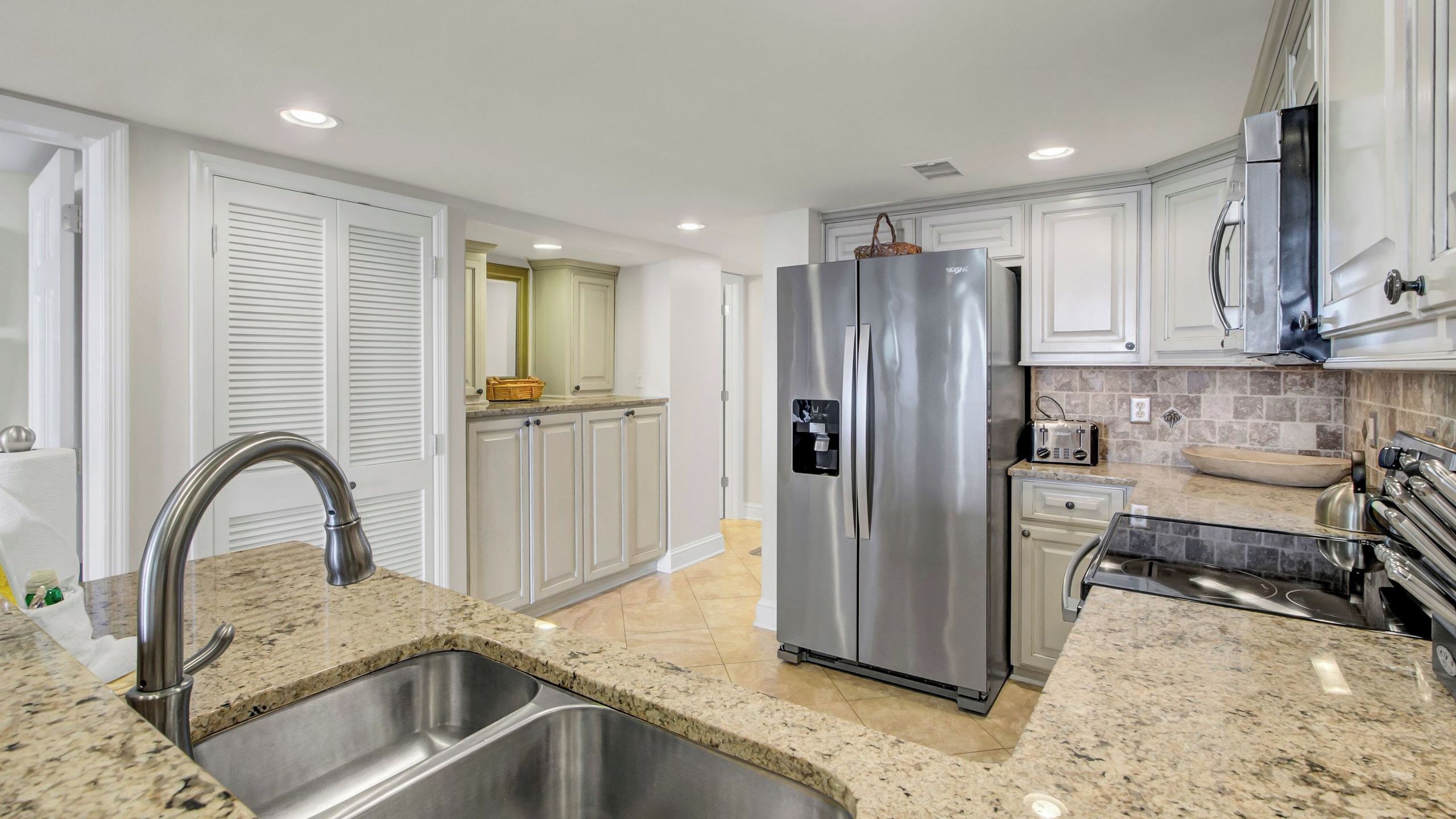 A modern kitchen with a stainless steel refrigerator, granite countertops, and white cabinetry.