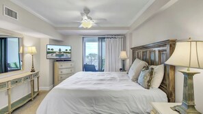 Een hotelkamer met een bed, een televisie, een dressoir, een plafondventilator en uitzicht op de omgeving.