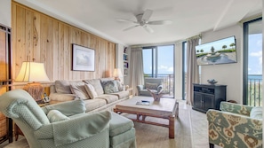 Een woonkamer met een bank, fauteuils, een salontafel, een televisie en een balkon met uitzicht.