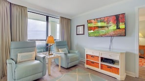 A living room with two light blue armchairs, a small table with a lamp, a glass cabinet with orange baskets, and a TV on the wall. - 311 Summerhouse by Avantstay Beach Views Access to Community Pool (Isle of Palms)