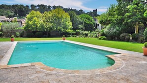 Piscina retangular com borda curva, rodeada por um terraço de pedra.