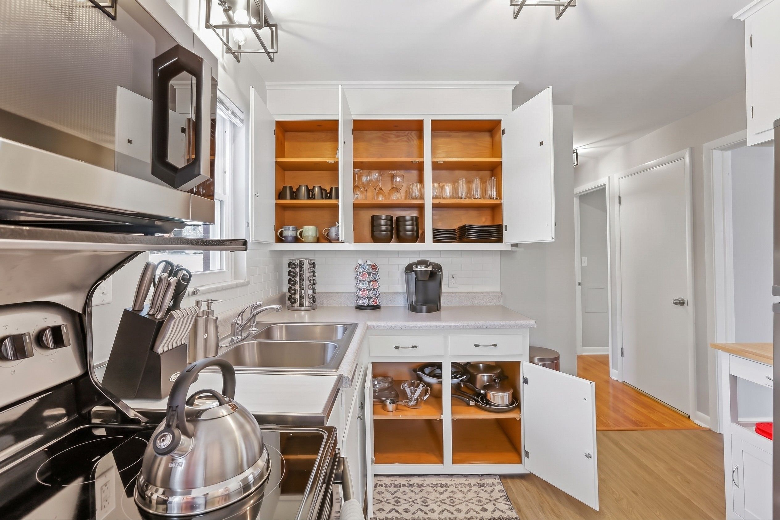 A modern kitchen with white cabinetry, a stainless steel kettle, and a coffee maker.