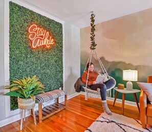 A cozy living room with a neon sign, a hanging chair, a side table with a lamp, and a green wall. - Comfy King Bed | Family Friendly | Games | Dogs OK (Columbus)