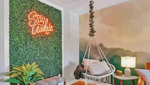 Ein gemütliches Zimmer mit einem Hängestuhl, einem kleinen Tisch mit Lampe und einem Neon-Leuchtschild an der Wand.