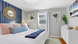 Ein modernes Schlafzimmer mit Bett, Nachttischen, einem Schminktisch und einem großen Spiegel, sowie Kunstwerken an den Wänden.