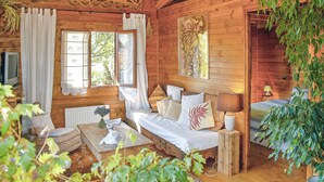 A cozy log cabin room with a wooden bed, a television, and a window with curtains.