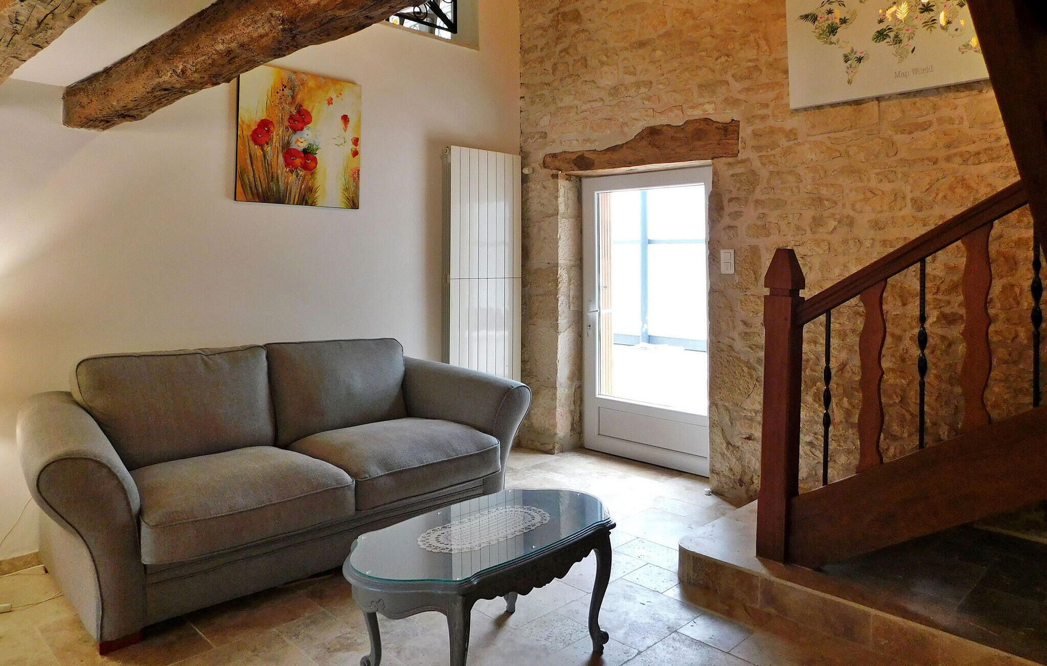A living room with a grey sofa, a glass coffee table, a wooden staircase, and a stone wall.