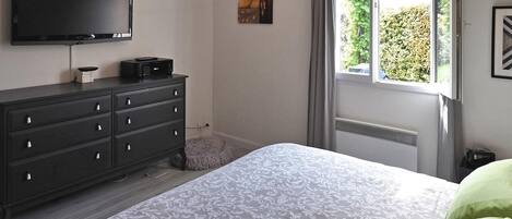 A bedroom with a bed, a dresser, a flat-screen TV, and a window with a view of greenery.