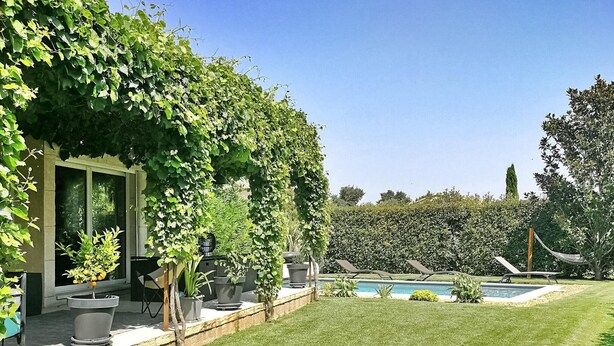 A well-maintained garden with a swimming pool, potted plants, and a grassy lawn.