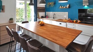 A modern kitchen with a wooden island, bar stools, pendant lights, and a blue accent wall.