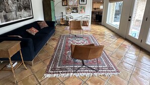 Een ruime woonkamer met een donkerblauwe bank, een bruine fauteuil en een kamerkleed met een patroon.