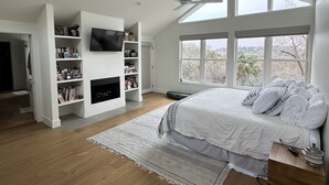 Een moderne slaapkamer met een groot bed, inbouwkasten, een flatscreen televisie en een open haard.