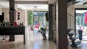 A modern kitchen with a central island, a dining area with a glass table, and a view of the outdoors. - La Villa De Sévigné (Rognonas)