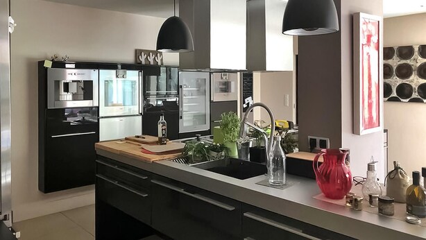 A modern kitchen with a black refrigerator, a built-in oven, a sink, and a wooden countertop. There are two pendant lights above the sink and a red vase on the countertop. - La Villa De Sévigné (Rognonas)