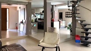 A spacious living area with a white armchair, a brown leather sofa, and a staircase with a modern design. - La Villa De Sévigné (Rognonas)