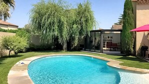 A swimming pool with a curved edge, surrounded by a well-maintained lawn and a variety of trees. - La Villa De Sévigné (Rognonas)