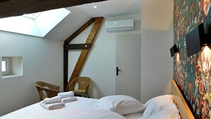 A bedroom with a skylight, a bed with white linens, a wicker chair, and a wall-mounted air conditioning unit. - Le Moulin De Lombraud (Brantome En Perigord)