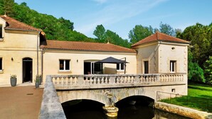 A two-story building with a balcony and a bridge over a water body. - Le Moulin De Lombraud (Brantome En Perigord)