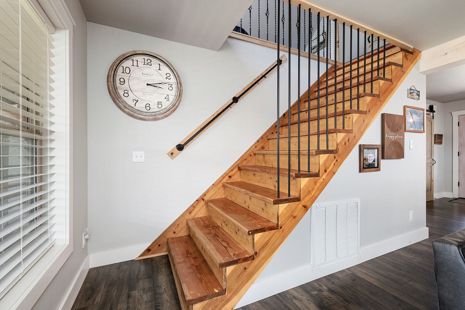 A wooden staircase with a black handrail, a wall clock, and a vent.