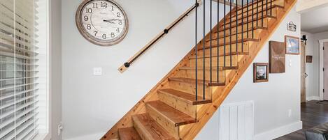 A wooden staircase with a black handrail, a wall clock, and a vent.